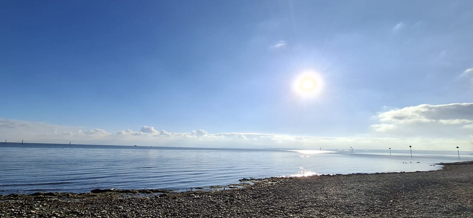 Blauer Himmel und die Sonne scheint über den Bodensee. Das Wasser ist ruhig und die Sonnenstrahlen schimmern auf dem See. 